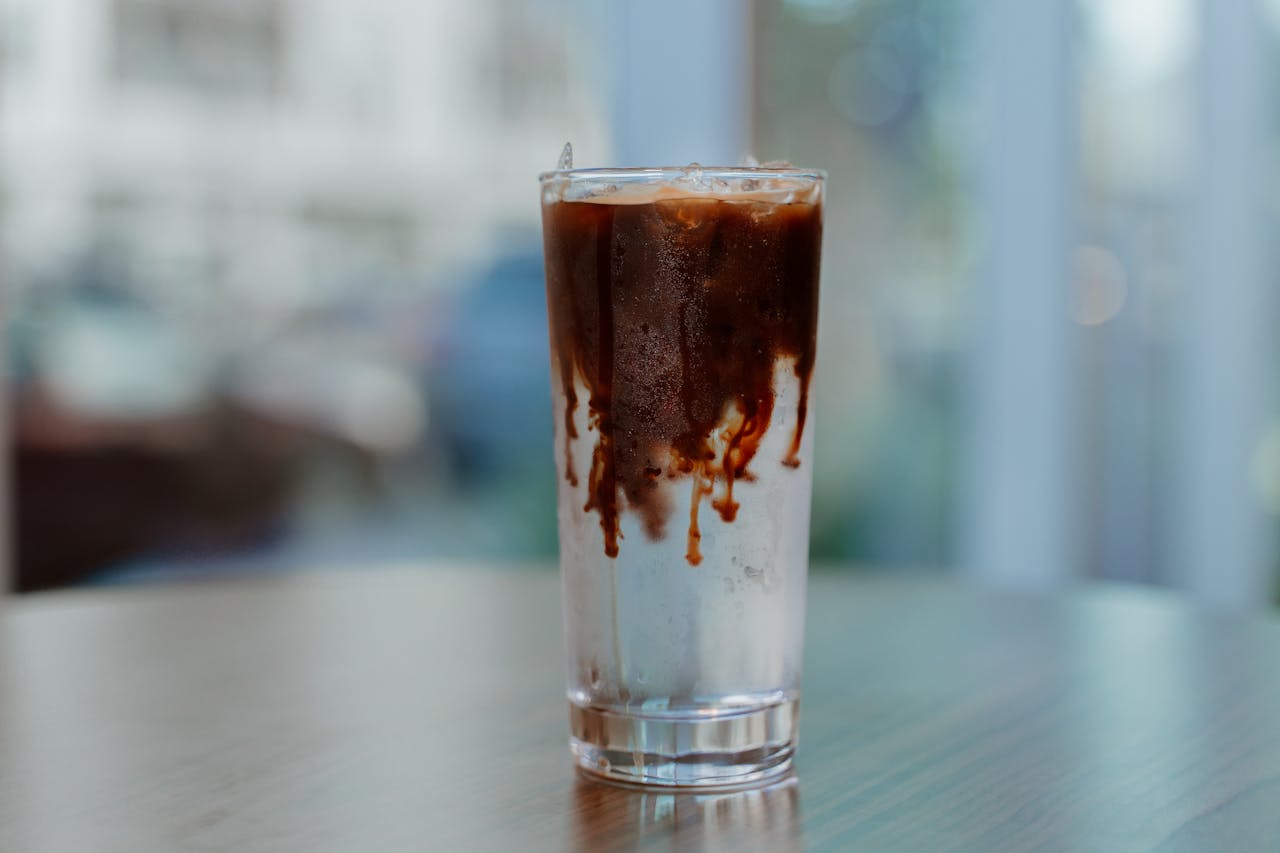 Refreshing glass of iced coffee with a creamy swirl on a wooden table indoors.